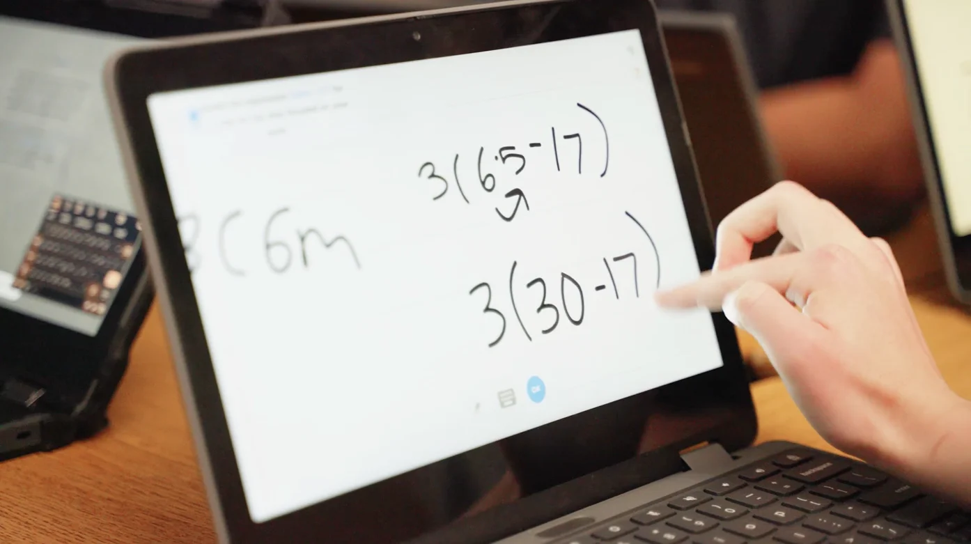 A student writing out the steps of 3(6 · 5 − 17) on a Chromebook whiteboard